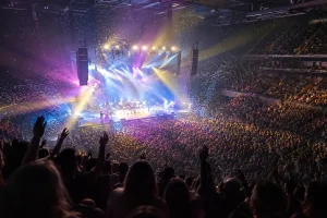 Fullsatt konsertarena med färgglada ljuskäglor och konfetti över scenen