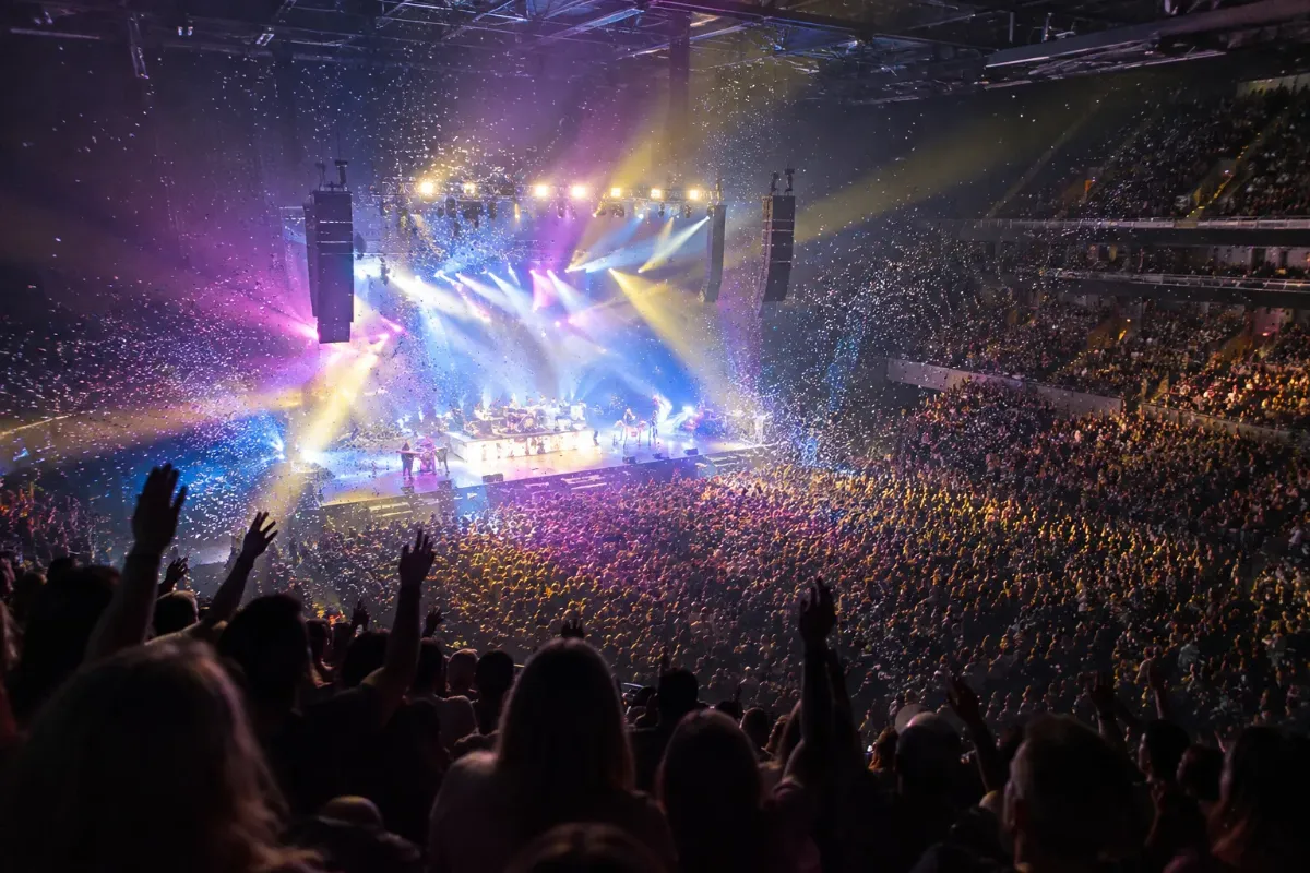 Fullsatt konsertarena med färgglada ljuskäglor och konfetti över scenen